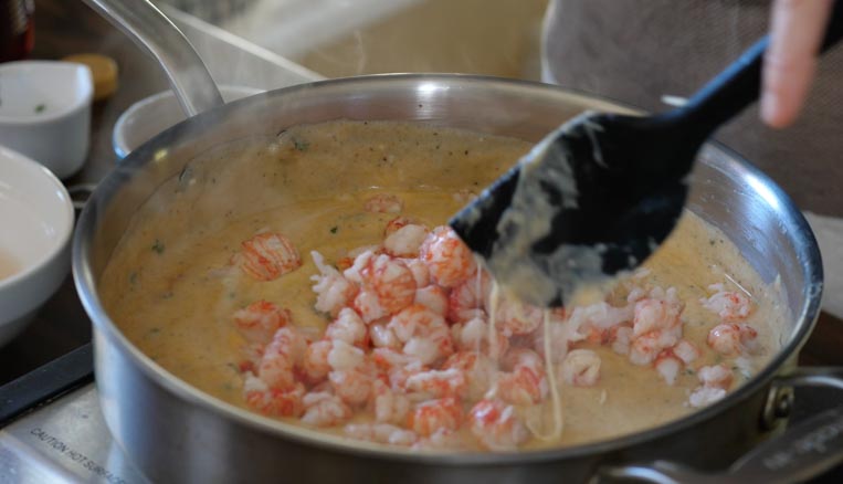 langostino lobster tails being stirred into cheese sauce 