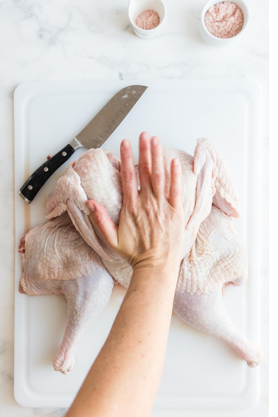 a hand pressing down between turkey breasts to flatten it