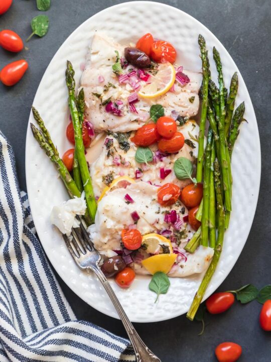 a platter of mediterranean baked fish with steamed asparagus