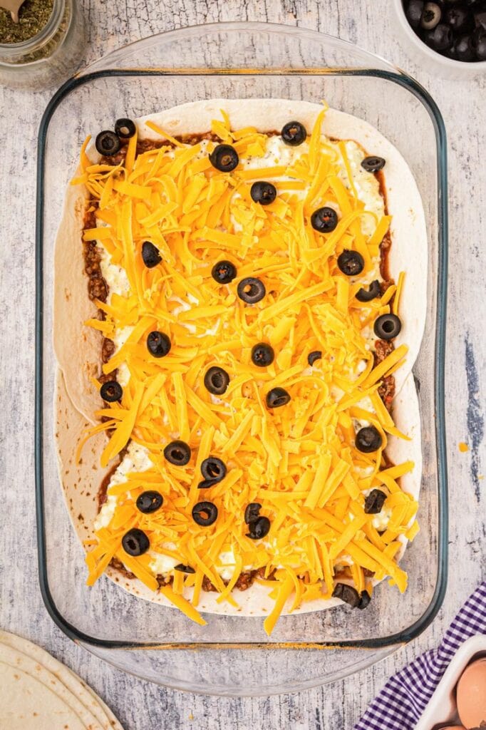 A 9x13 pan with flour tortillas, meat sauce, cottage cheese, cheddar cheese and black olives 