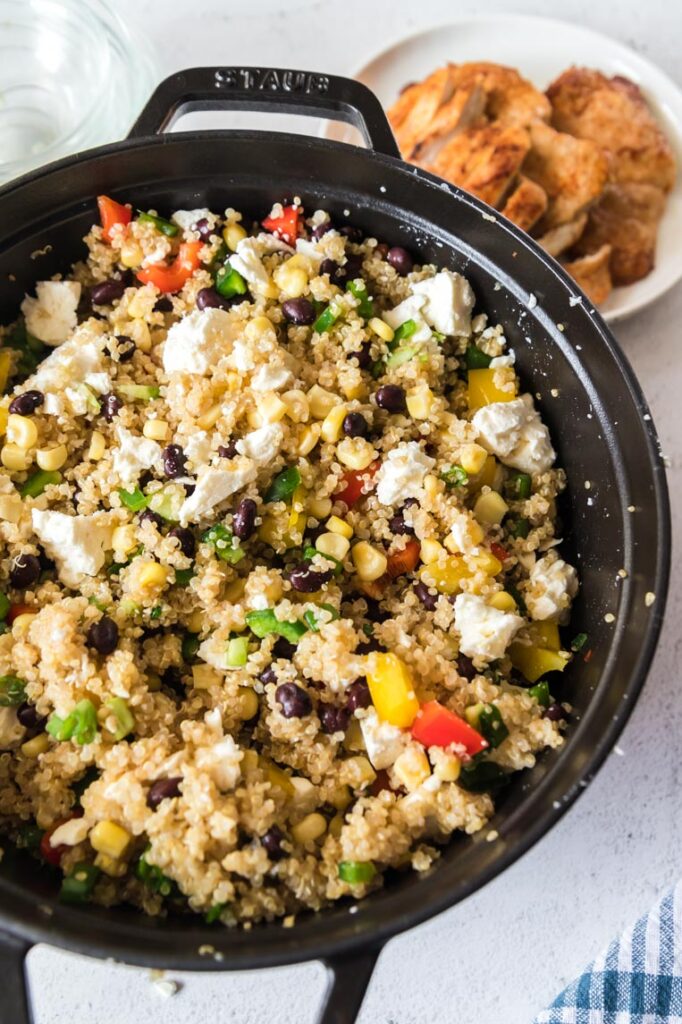 a black pot of quinoa mixed with vegetables and cotija cheese