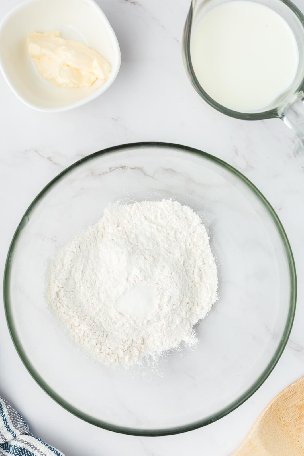 a bowl of flour and sugar on a table with two smaller bowls of mayonnaise and milk