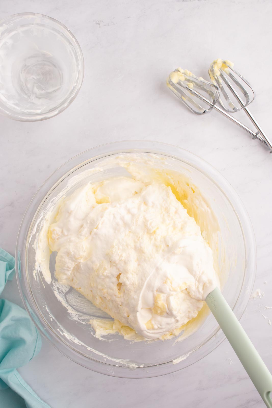 a bowl with a spatula folding cool whip or whipped cream into the pineapple mixture 