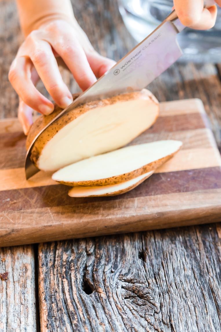 a knife slicing thick slices of a whole potato