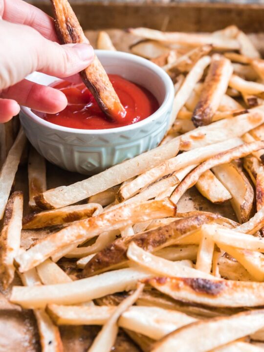 a hand dipping a fry in ketchup