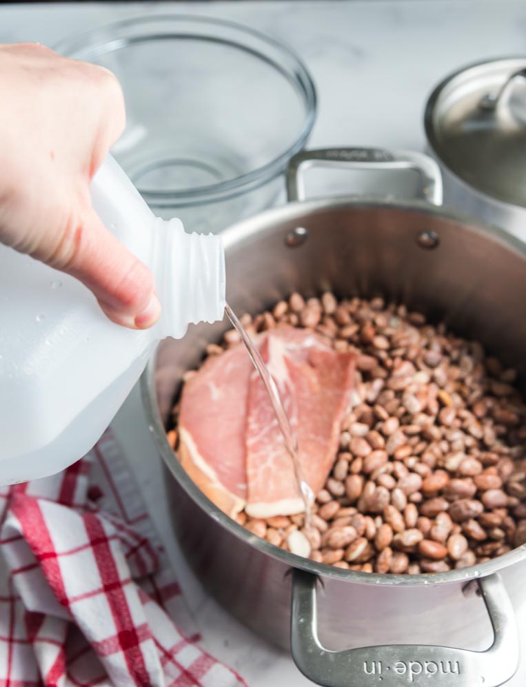 adding water from a jug to a pot of pinto beans