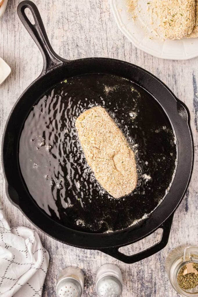 A skillet with a pork chop frying in oil 