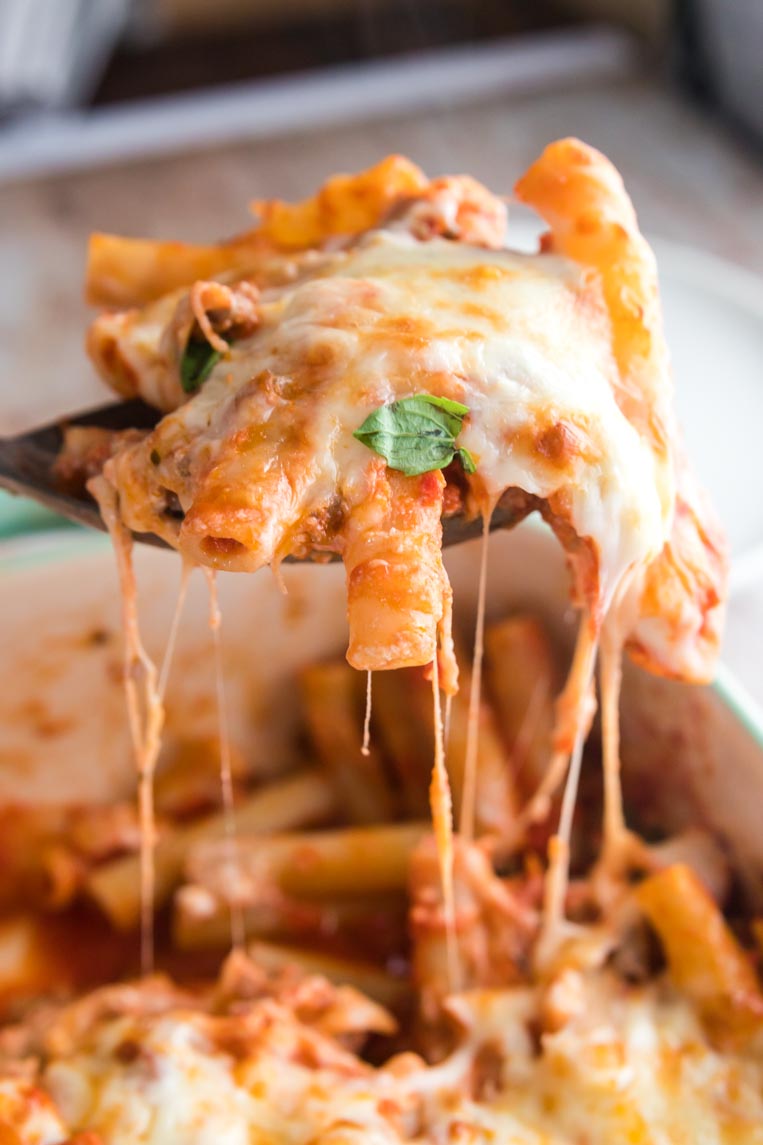 a spoonful of baked ziti being lifted from the pan on a spoon with strings of cheese