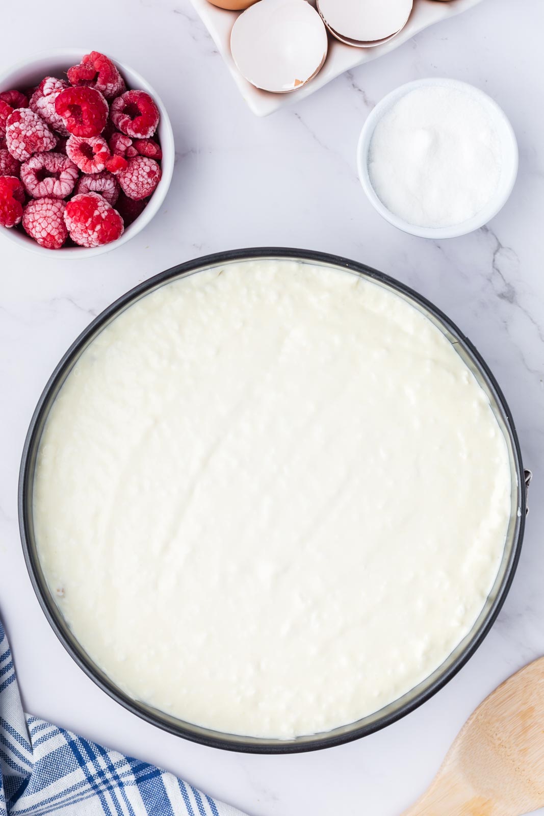 Cheesecake filling in a springform pan ready to be bakes. Frozen raspberries standby.