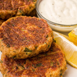 salmon patties on a plate with lemons and sauce