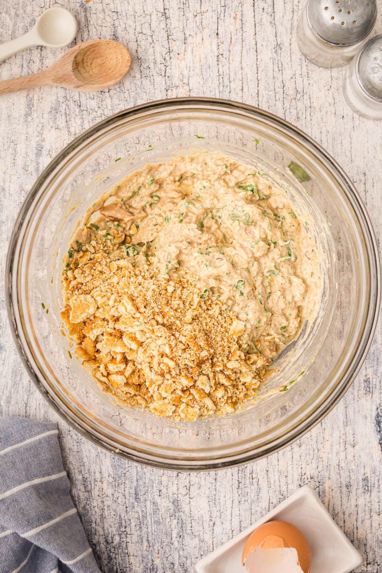 A bowl of salmon that has been mixed with spices, eggs, mayonnaise and cracker crumbs are added.