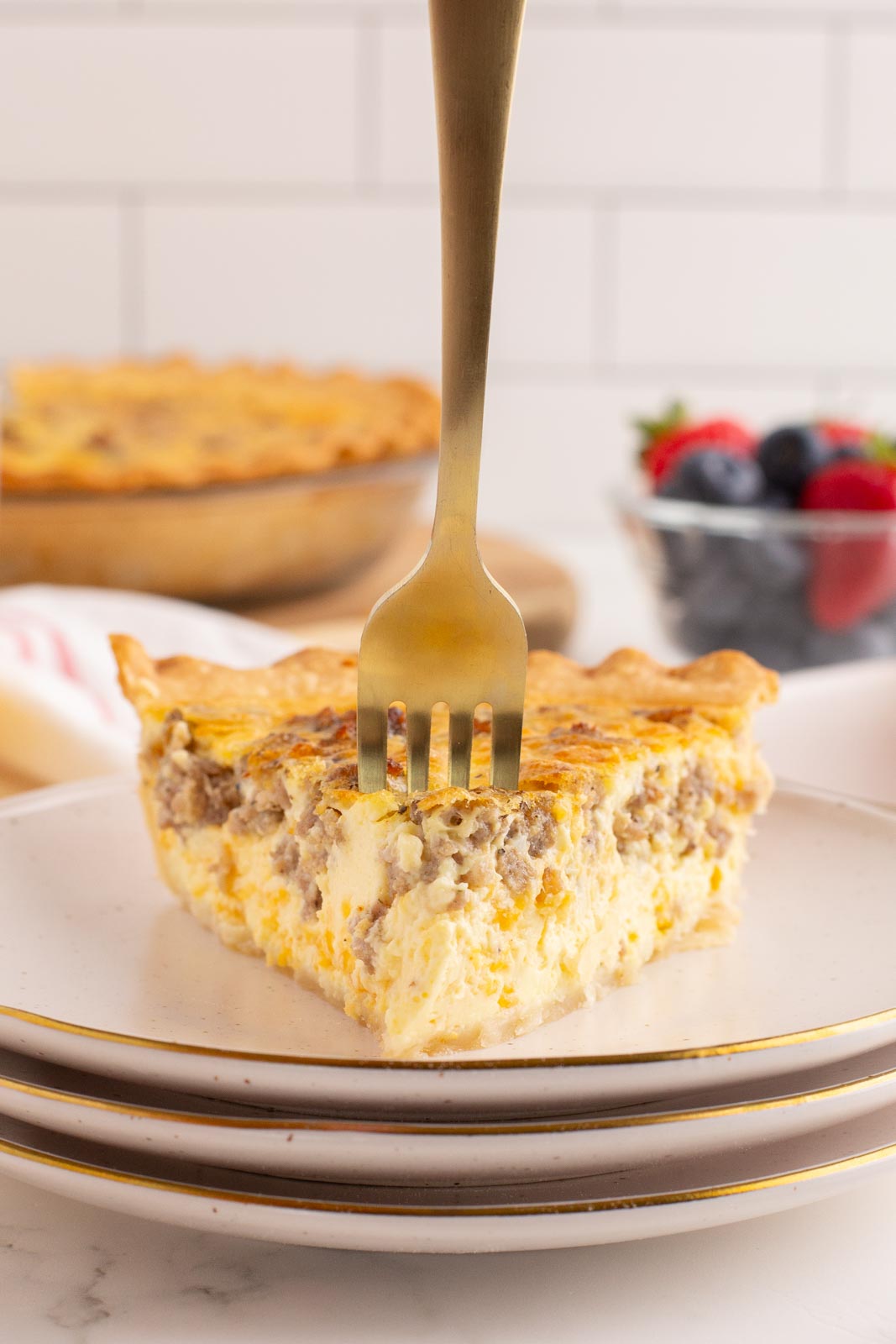 a slice of sausage and egg quiche on a plate with a fork in it