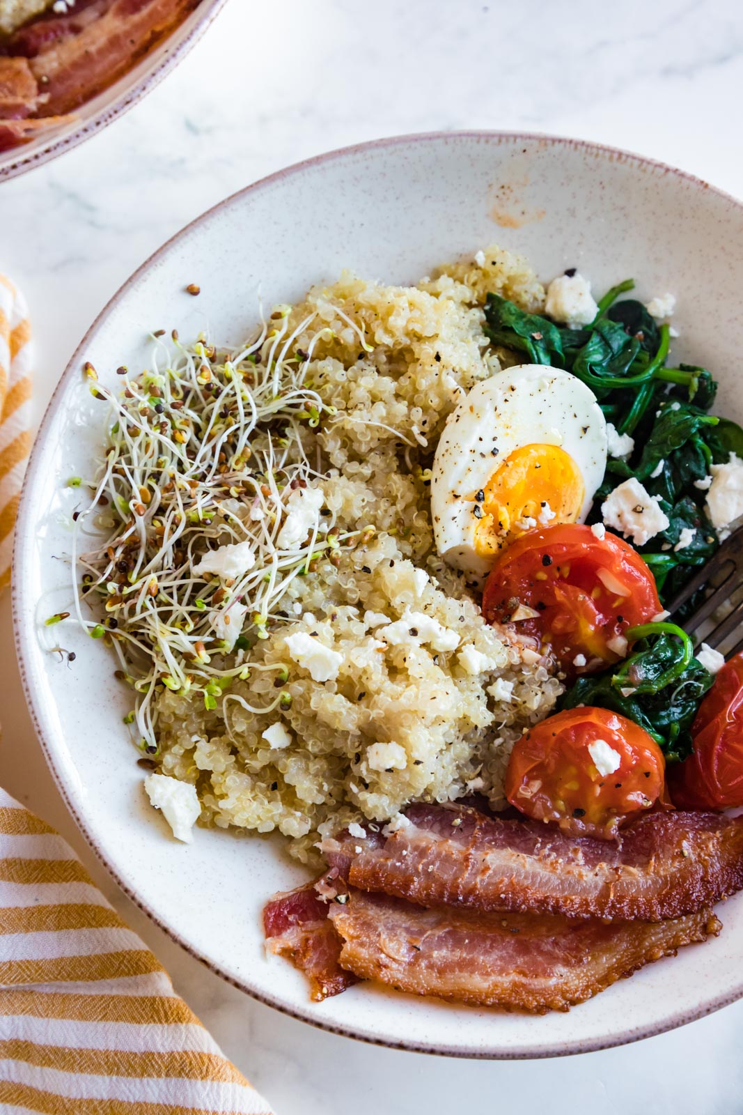 a bowl of breakfast foods with quinoa, tomatoes, bacon, eggs 