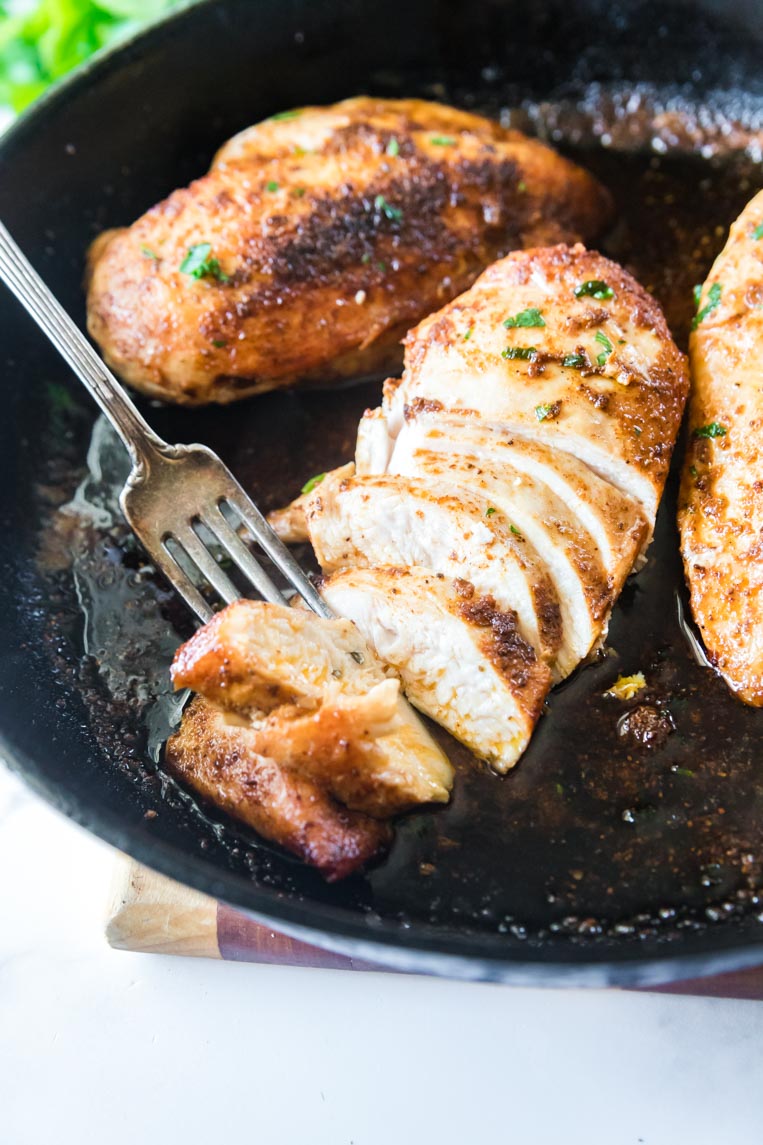 sliced chicken breasts in a skillet with a fork
