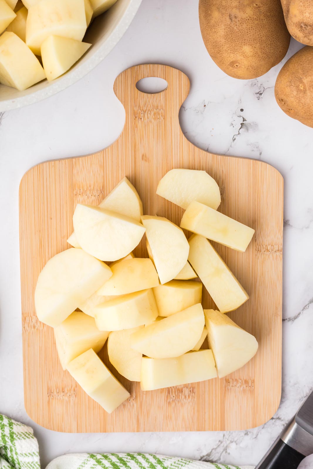 a cutting board with cubed potatoes waiting to be boiled. 