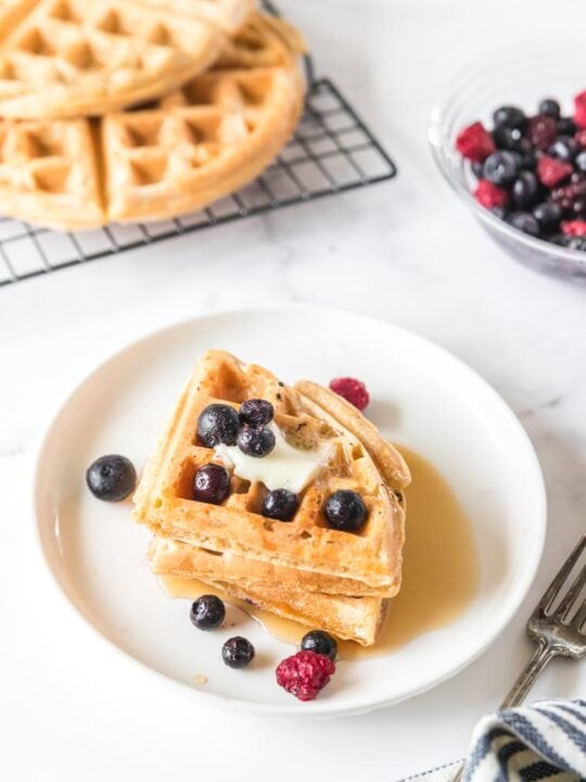 three triangular waffles on a white plate with butter and berries