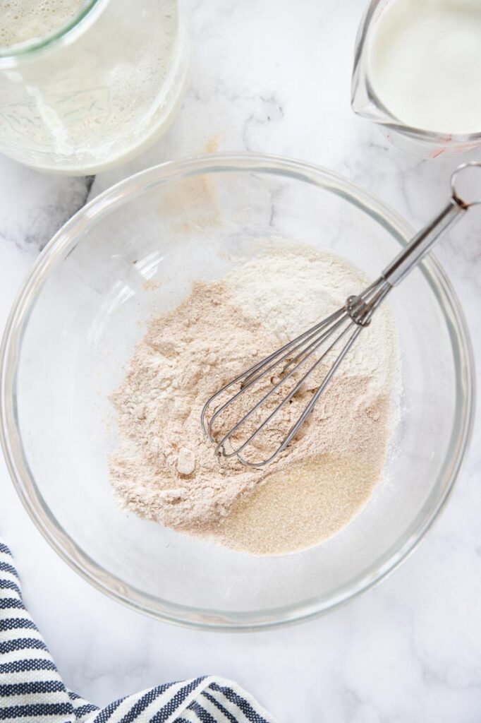 A bowl of flour and sugar in a on a white table with a whisk 