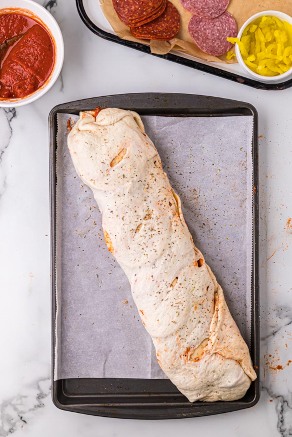 a rolled but unbaked stromboli on a rimmed cookie sheet