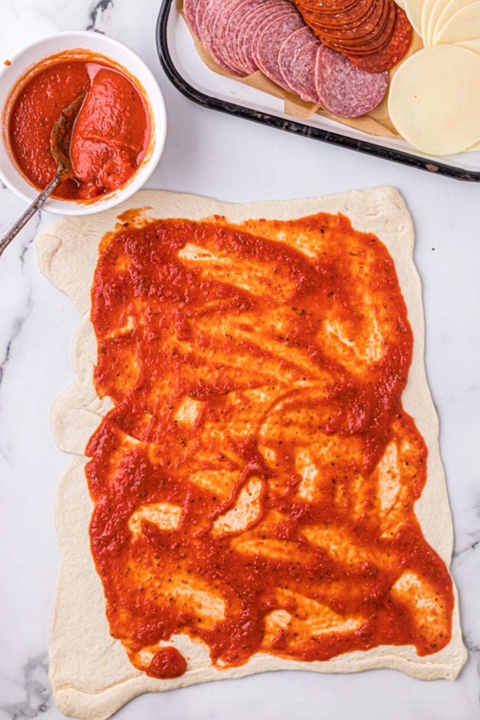 a rectangle of pizza dough on a board with sauce spread on 