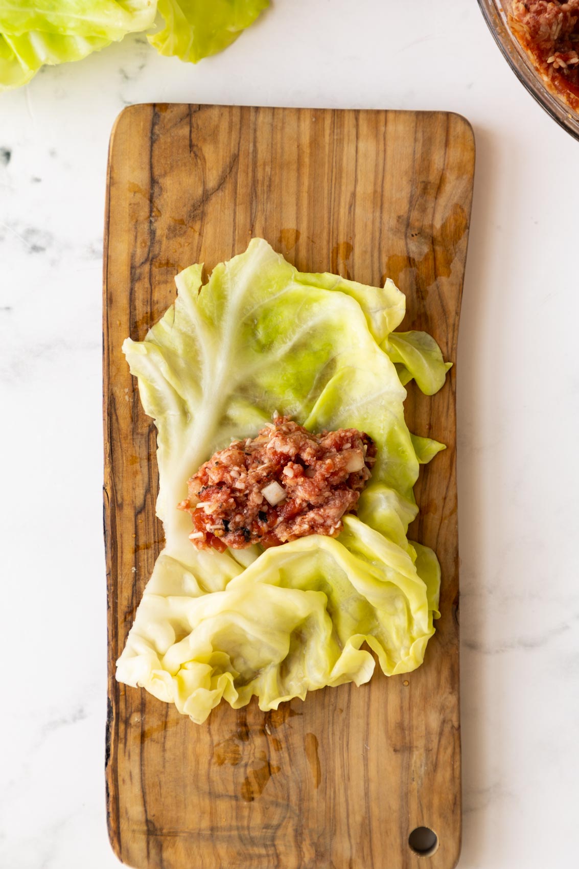 a length of cabbage on a cutting board with a small amount of beef filling in the center