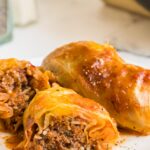 a plate of cooked stuffed cabbage rolls on a plate with one sliced open to show filling