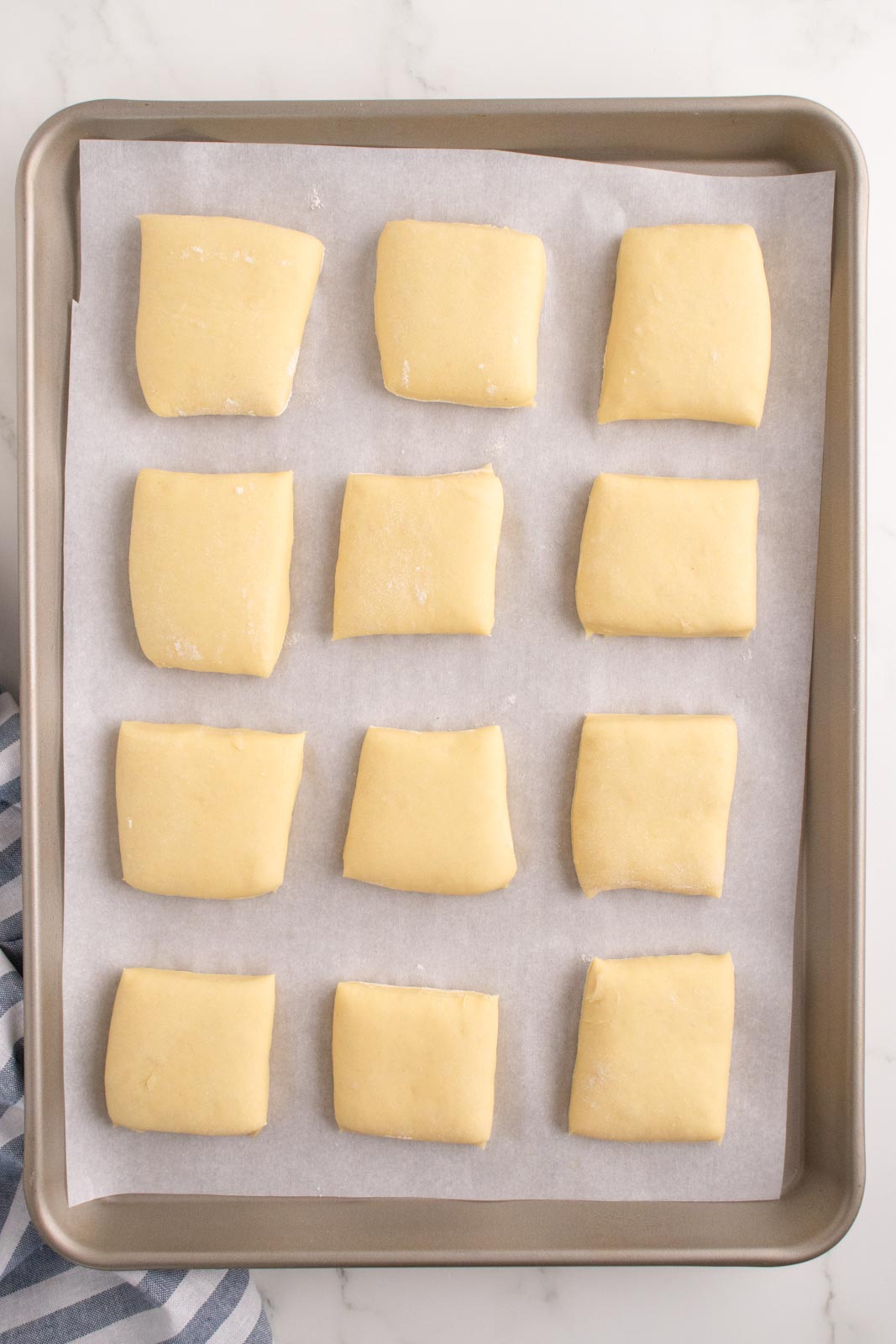 Squares of dough arranged on a baking sheet lined with parchment paper.