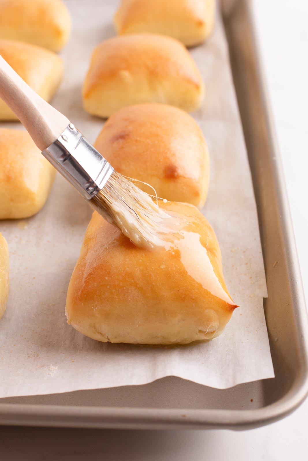 Brushing baked Texas roadhouse rolls with butter.