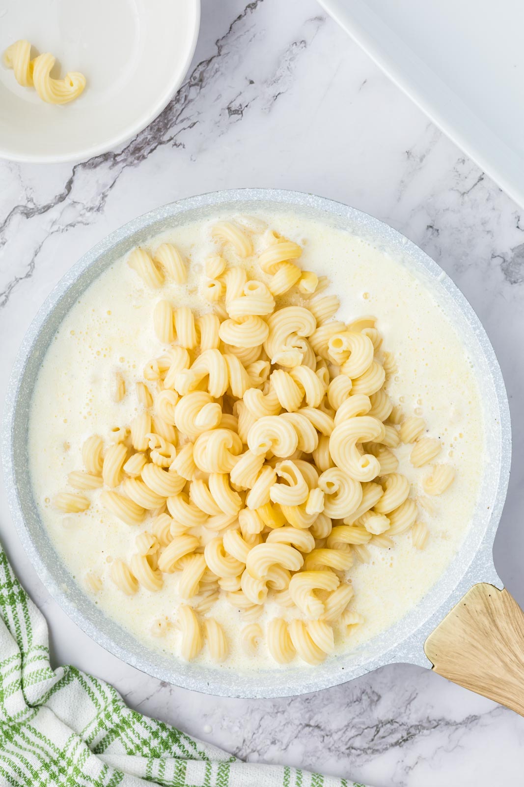 Adding cooked macaroni noodles to cheesy white sauce to make baked white mac and cheese.