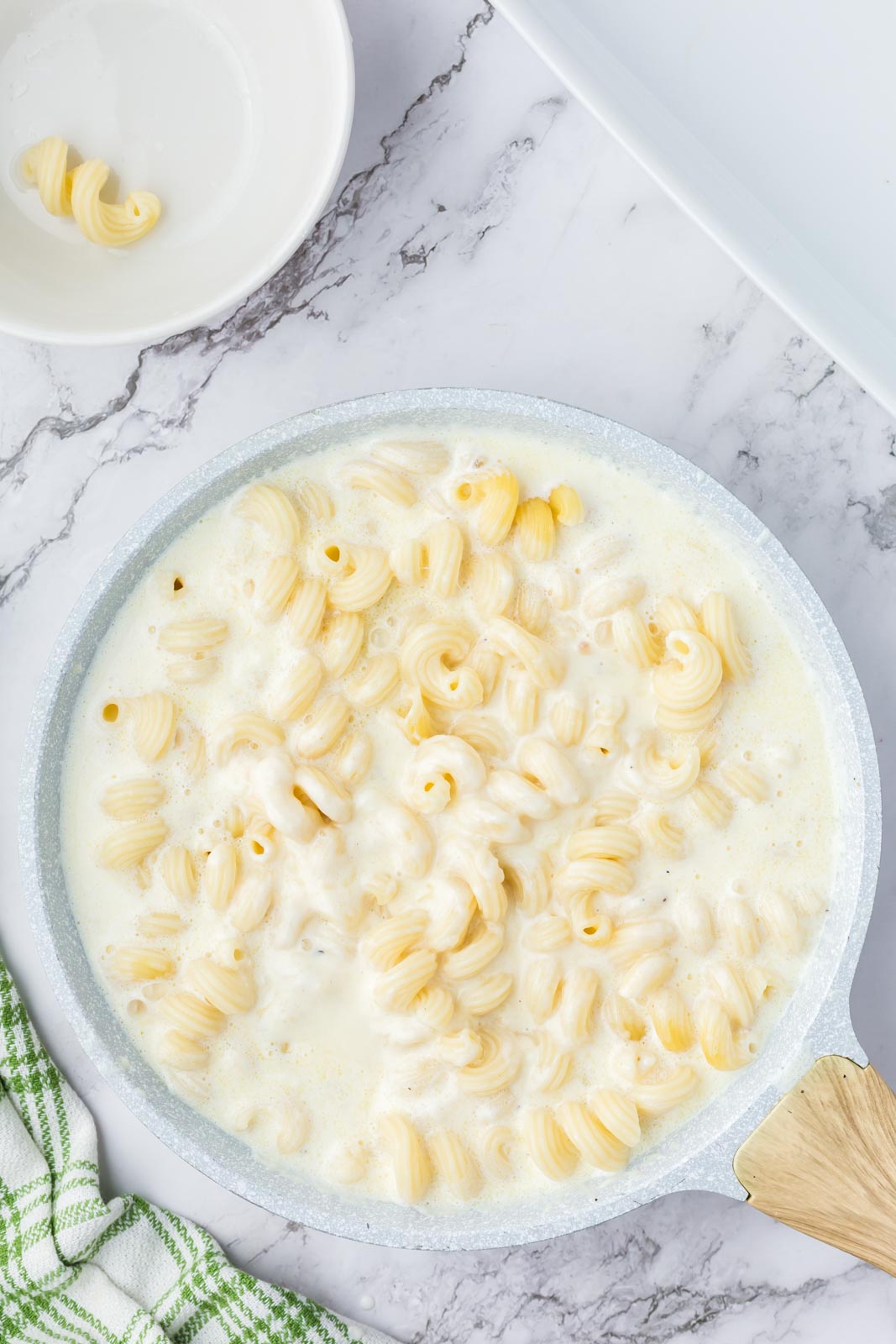 Coating macaroni noodles in cheesy white sauce.