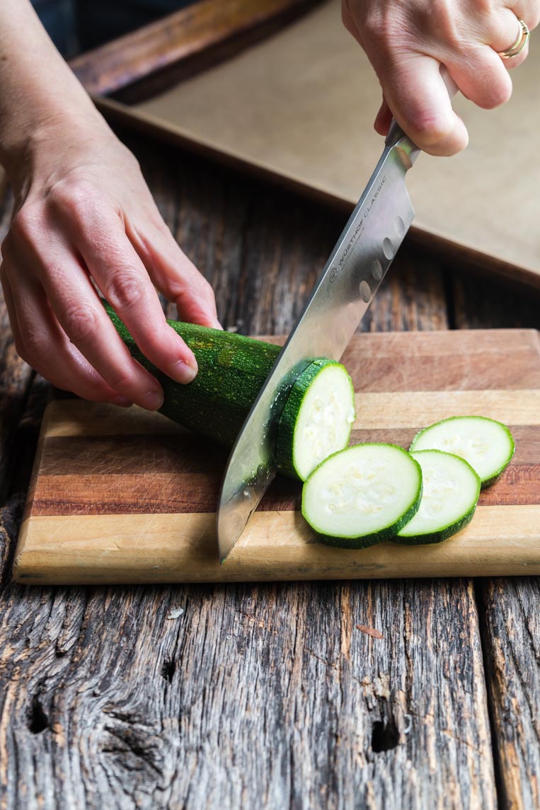 a zucchini on a cutting board with a knife cutting a slice