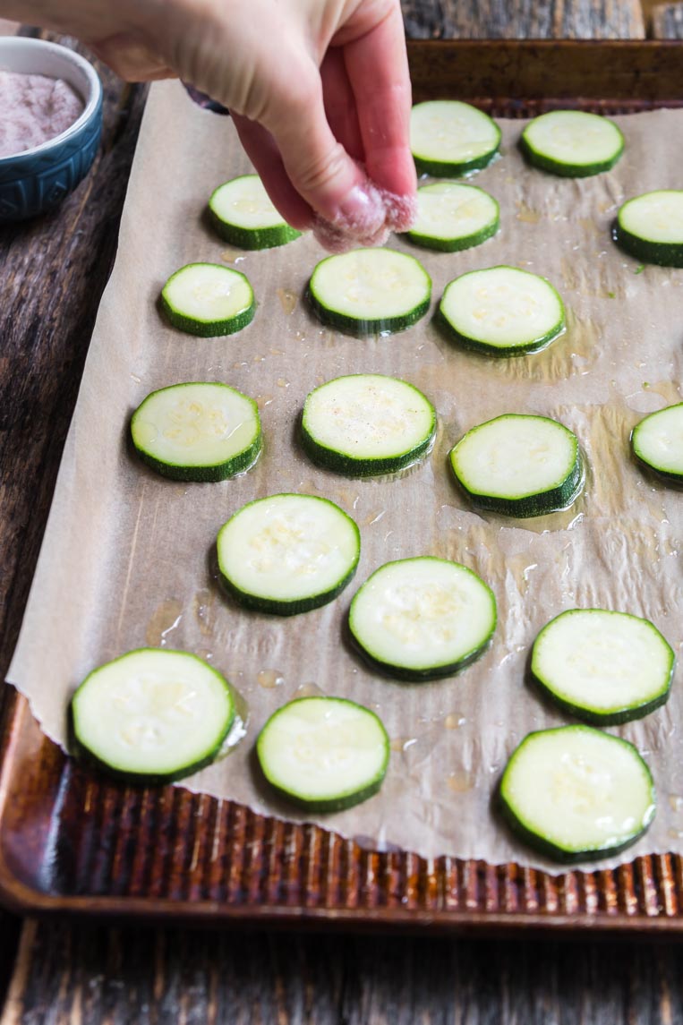salt being sprinkled over zucchini on a cookie sheet