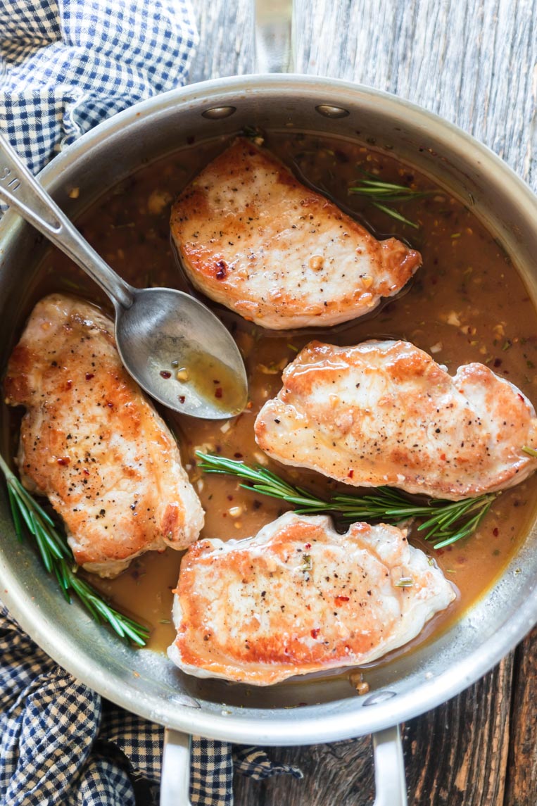 four pork chops in a skillet with a spoon