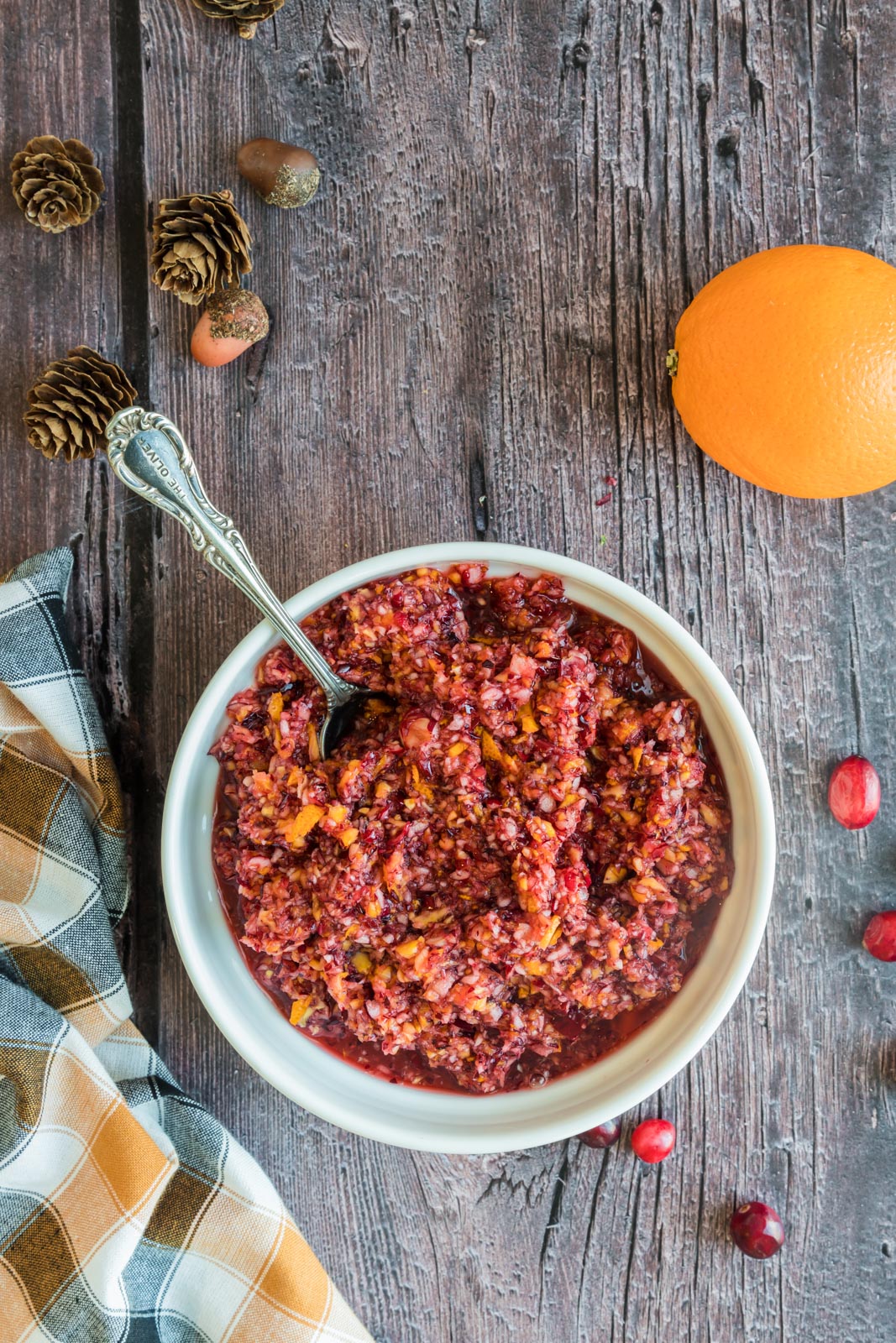 a bowl of cranberry orange relish on a table with an orange and a spoon in the bowl
