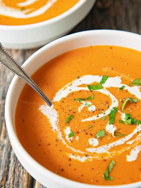 a bowl of creamy tomato bisque on a table with a spoon in the soup