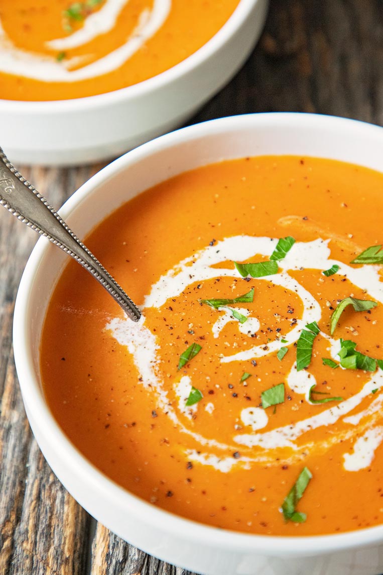a bowl of creamy tomato bisque on a table with a spoon in the soup 