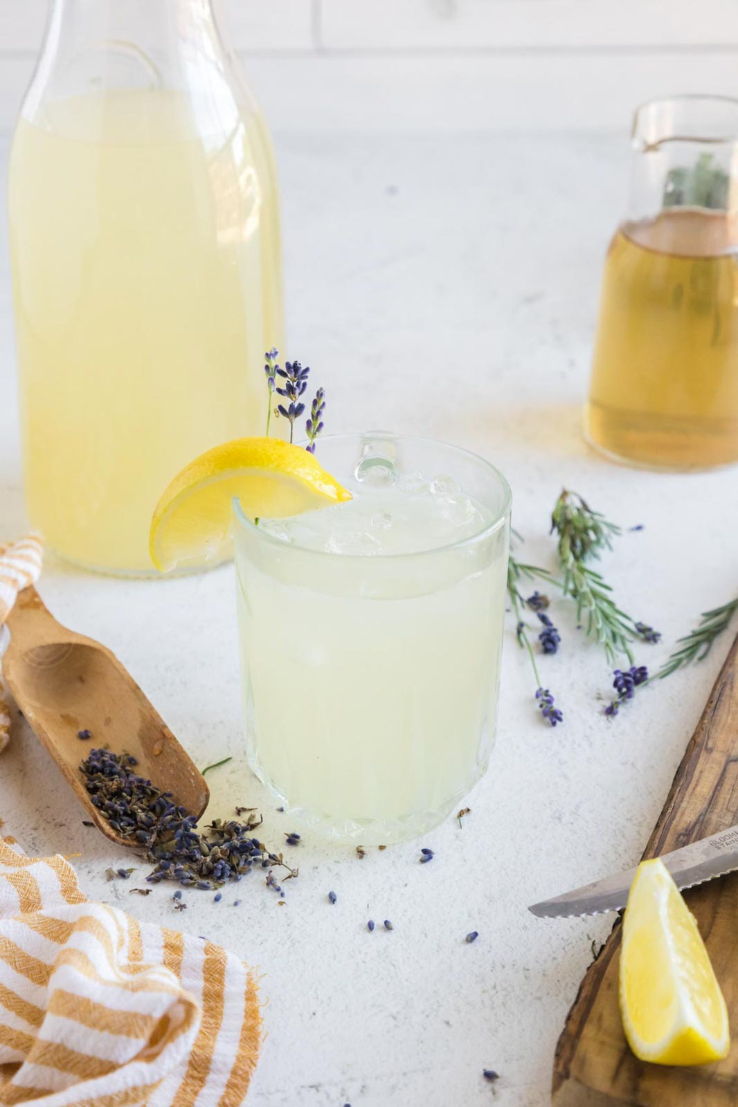 Iced lavender lemonade in a glass near fresh lavender, dried lavender, lemon, and lavender simple syrup.