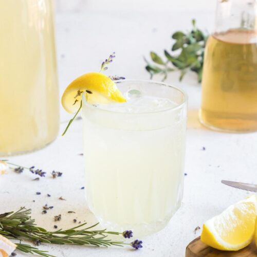 Iced lavender lemonade in a glass garnished with fresh lavender and a lemon wedge.