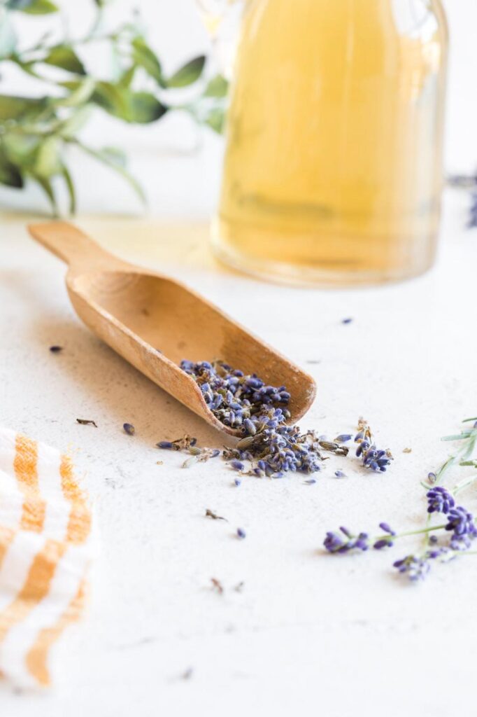 Fresh lavender buds in a wooden scoop with lavender syrup in the background.