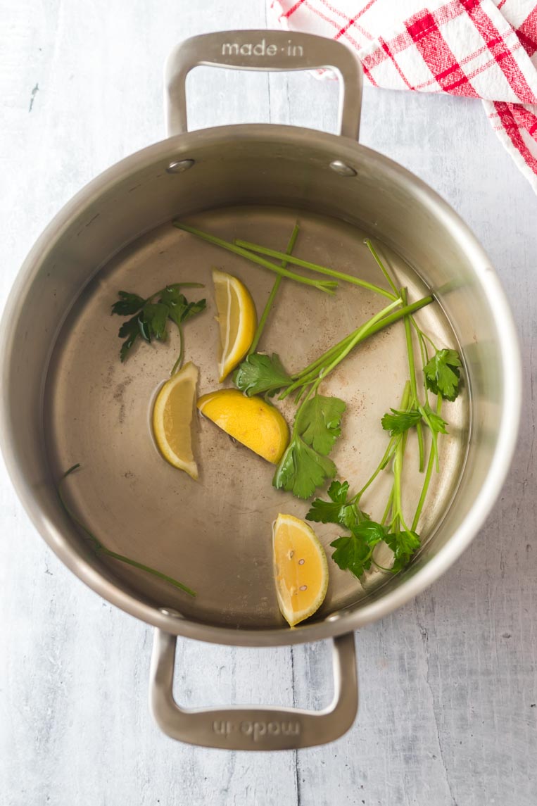 a pot with parsley stems and lemon in cooking liquid 