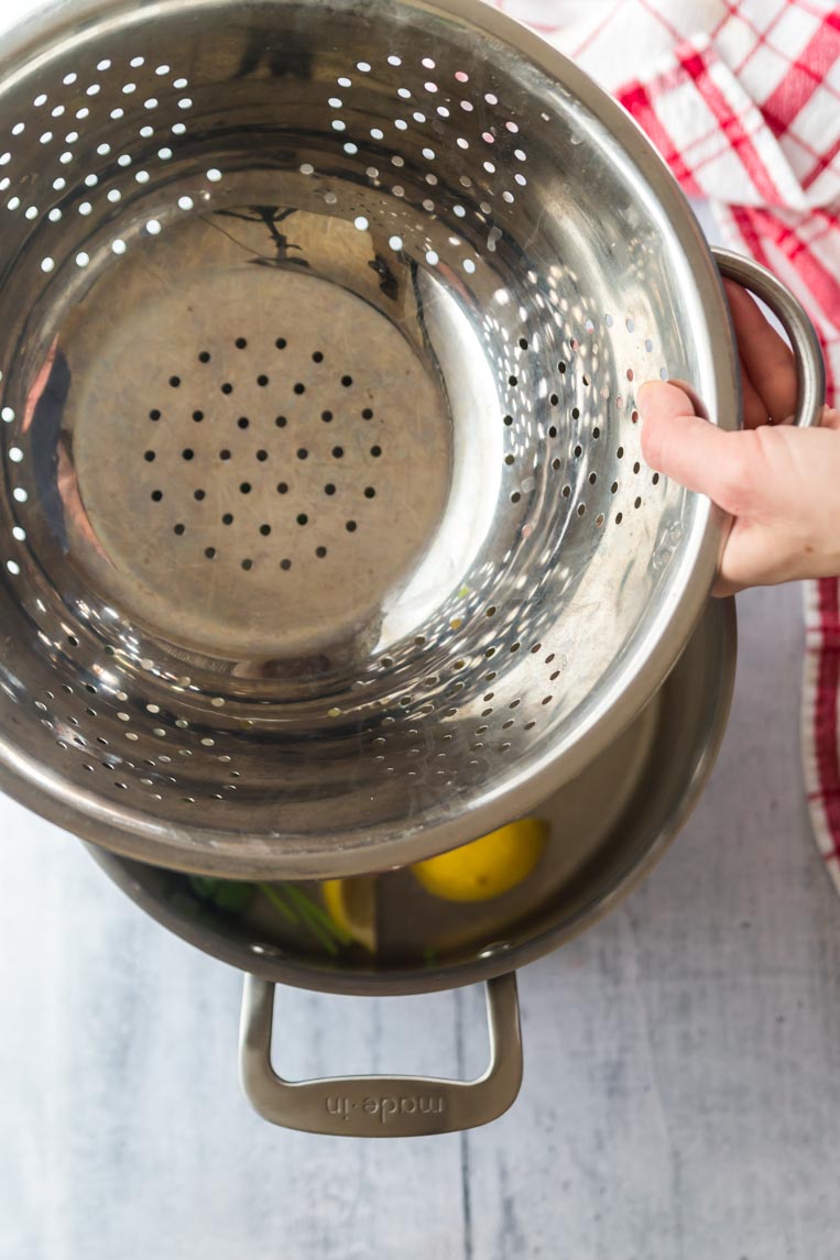 a metal colander being placed over a pot of simmering water