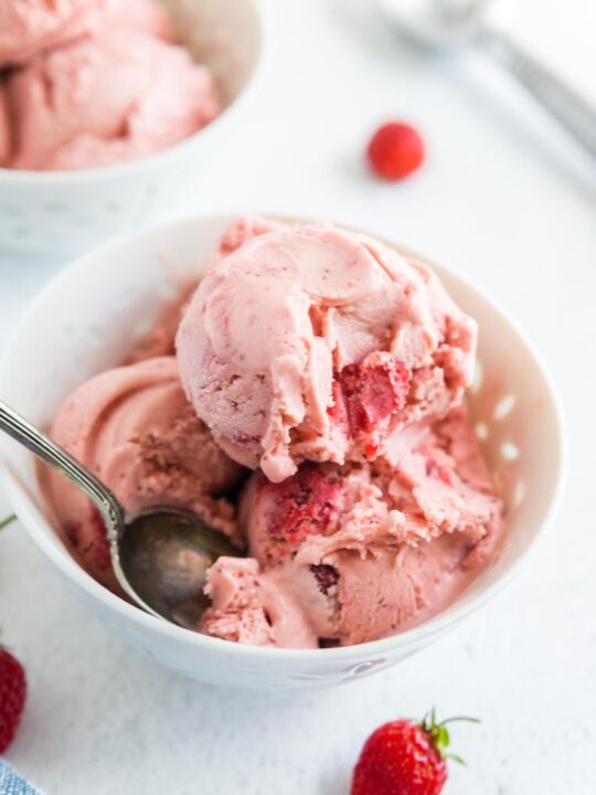 a bowl of scooped strawberry ice cream on a table