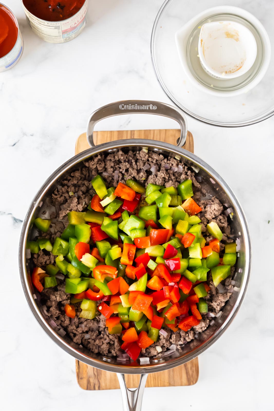 a skillet with diced green and red bell peppers added to cooked ground beef 
