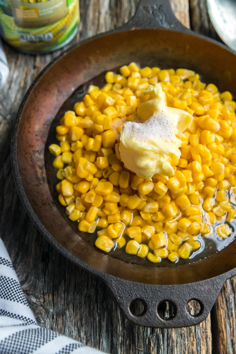 a skillet of canned corn with butter and salt on top before cooking
