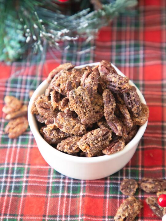 a bowl of easy candied pecans on a red plaid tablecloth with holiday greenery