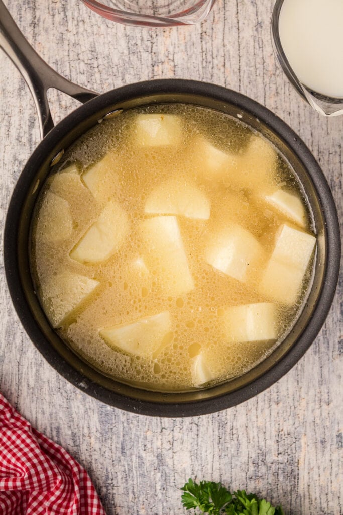 Potatoes covered with chicken stock in a pot.