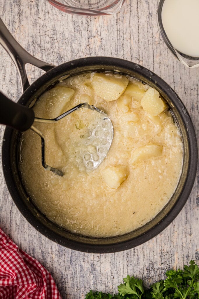 Potatoes with a hand masher in a pot.  