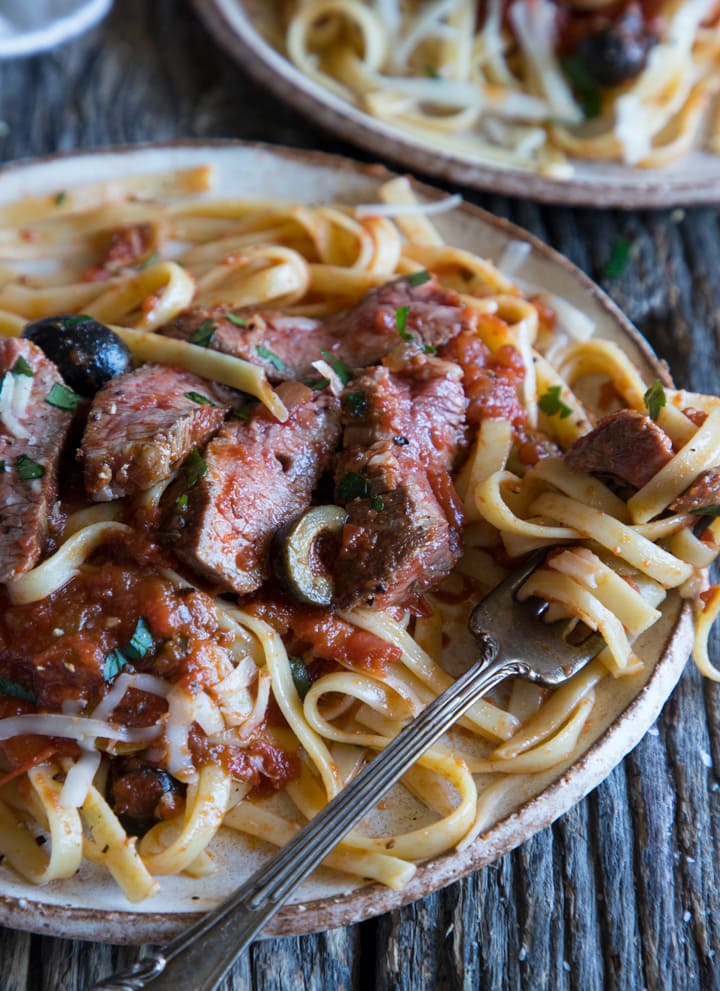 close up of sliced steak on pasta with olives