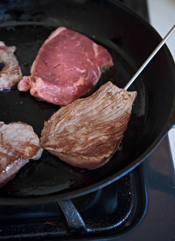 checking the internal temperature of steaks searing in a skillet