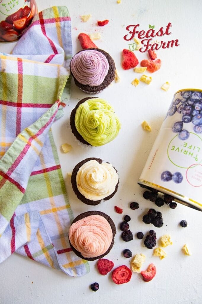 four cupcakes in a line with open cans of freeze dried fruit on a table with a colored napkin 