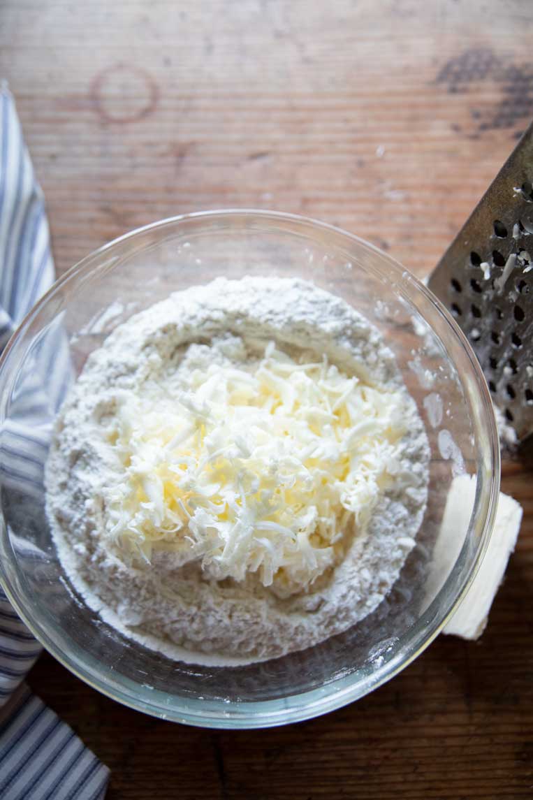 a bowl of flour with a pile of grated butter piled in the center
